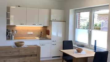 A modern kitchen with white cabinets, a wooden dining table, and a window with a view of the outside.