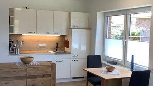 A modern kitchen with white cabinets, a wooden dining table, and chairs. - Ferienwohnung in Burhave (Butjadingen)