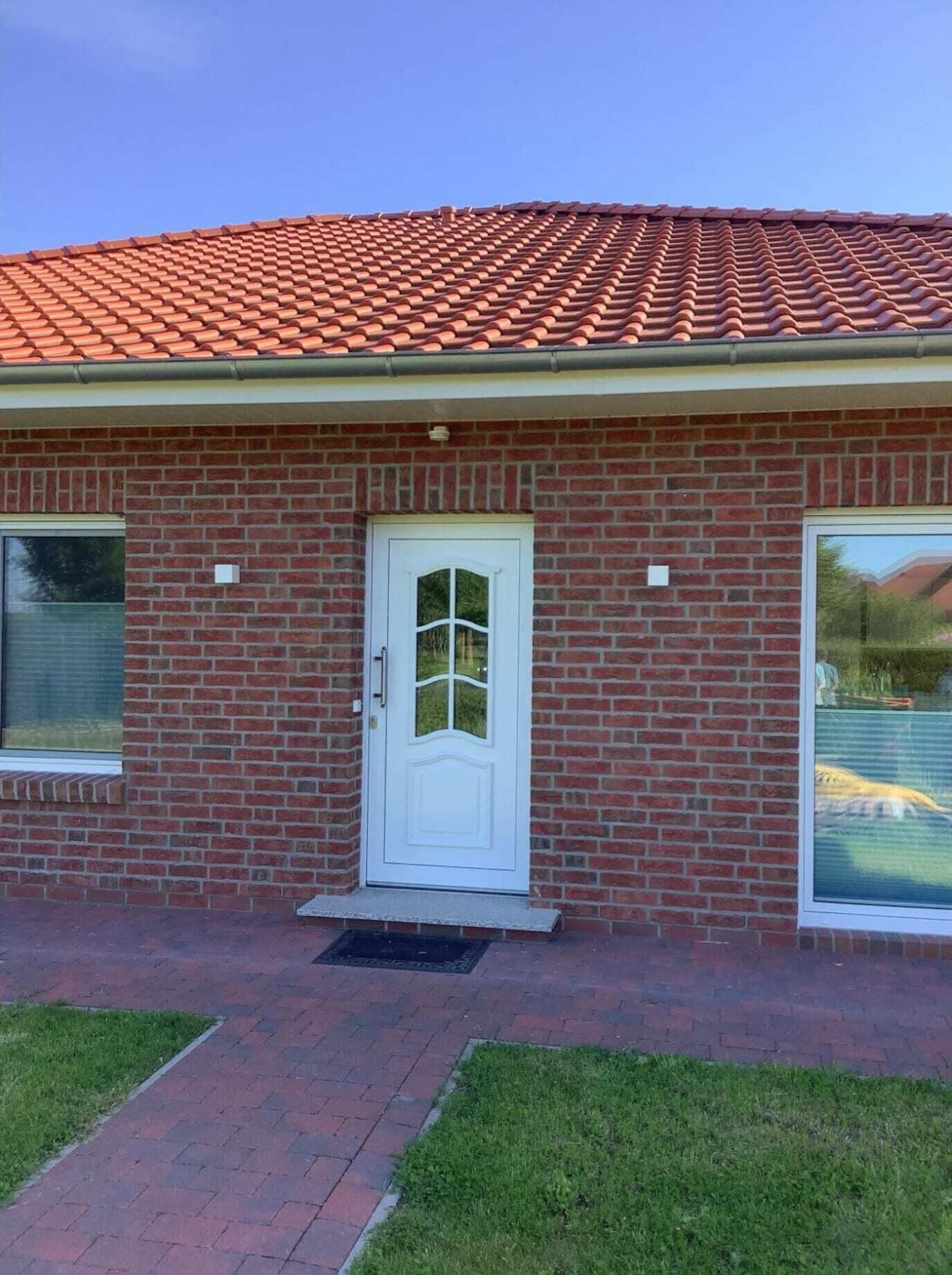 A single-story brick building with a red-tiled roof, a white front door, and a small front porch.