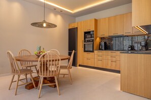 A modern kitchen with wooden cabinets, a central island, and a dining area with a round table and chairs. - Athena’s Luxury 3-Bedroom Villa with Private Pool & Garden in Koskinou of Rhodes (Koskinou)