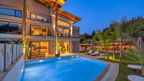 Una casa moderna de dos pisos con piscina, mobiliario exterior y un patio bien iluminado.