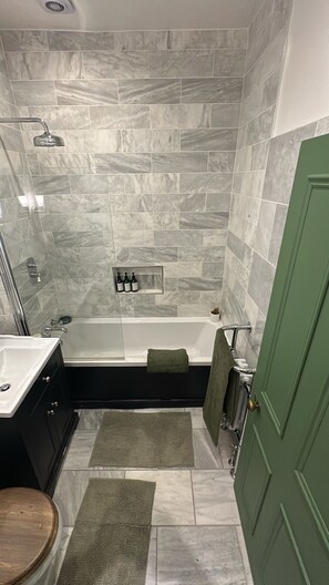A bathroom with a bathtub, shower, and sink. There are towels and toiletries visible. - Cosy West Kensington Apartment - 3 Min to Tube (London)