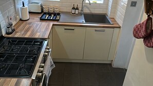 A compact kitchen with a gas stove, a sink, and a window providing natural light. - Cosy West Kensington Apartment - 3 Min to Tube (London)