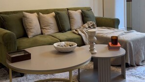 A living room with a green sofa, two round coffee tables, a floor lamp, and a painting on the wall. - Cosy West Kensington Apartment - 3 Min to Tube (London)