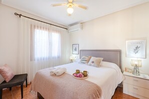 A neatly arranged bedroom with a large bed, a bedside table with a lamp, a chair, and a window with sheer curtains. - Flamenca Beach by Fidalsa (Orihuela)