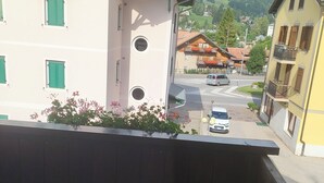 A balcony with a view of a mountain, a street with cars, and buildings with balconies. - Suite in Hotel Cristallino (Cortina d'Ampezzo)