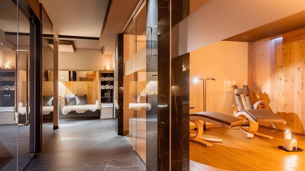 A modern spa area with a massage table, wooden flooring, and a glass partition. - Suite in Hotel Cristallino (Cortina d'Ampezzo)