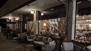 An outdoor seating area with wicker furniture, a brick floor, and a view into the restaurant. - Suite in Hotel Cristallino (Cortina d'Ampezzo)
