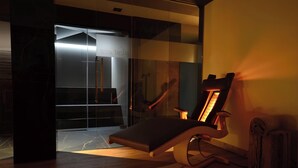 A modern spa room with a massage chair, a sauna, and a glass-enclosed shower area. - Suite in Hotel Cristallino (Cortina d'Ampezzo)