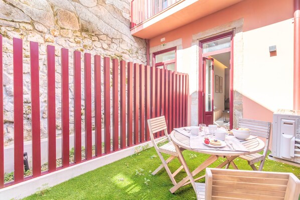 A patio with a table set for dining, a stone wall, and a red fence. - Caldeireiros 95 by LovelyStay (Porto)