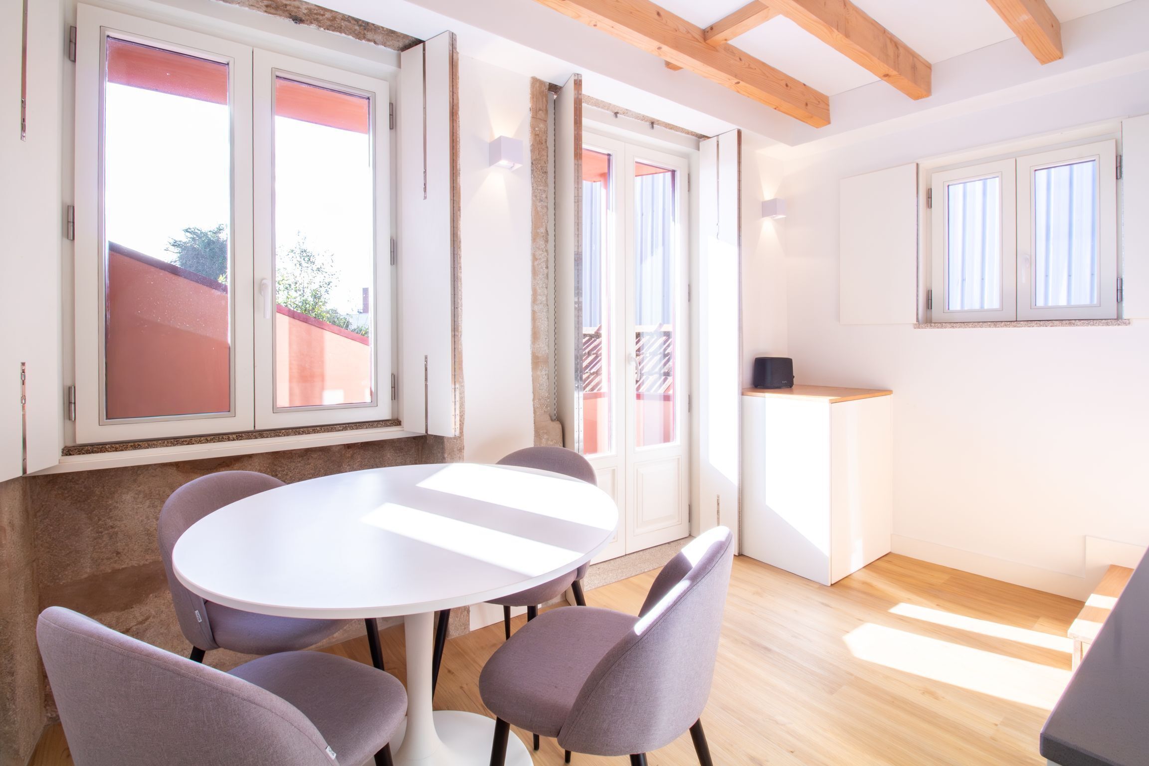 Ein Zimmer mit einem runden Tisch, vier Stühlen, einer kleinen Theke und großen Fenstern.