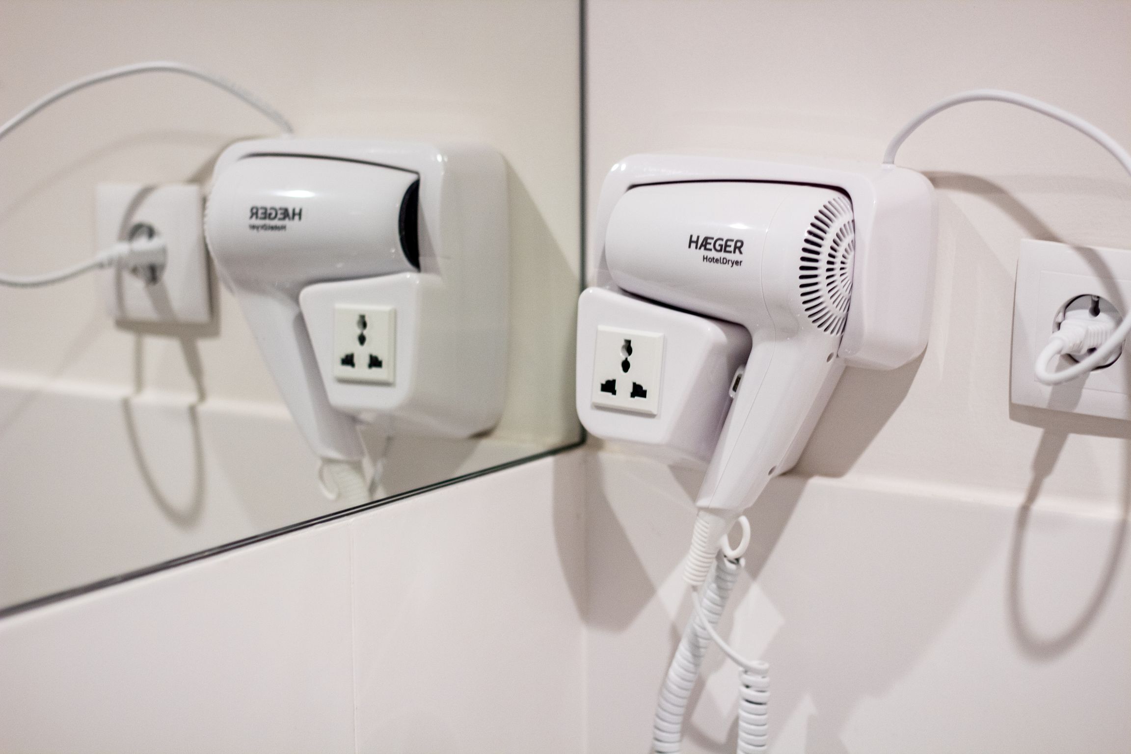 A hotel room with a mirror reflecting a hairdryer and a plug.