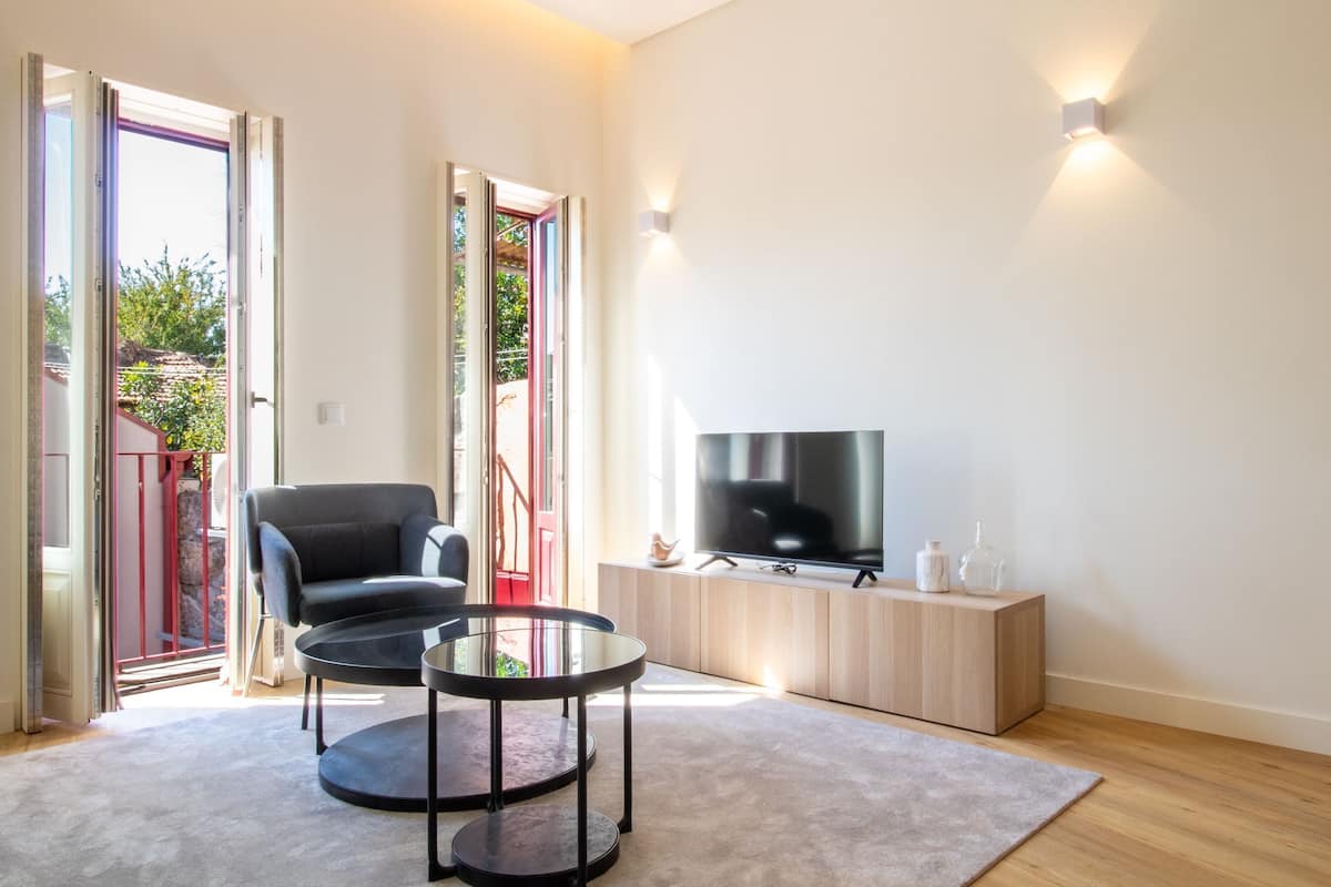 Una sala moderna con un sillón negro, una mesa de centro de vidrio, un televisor sobre un mueble de madera y un ventanal corredero que da a un espacio exterior.