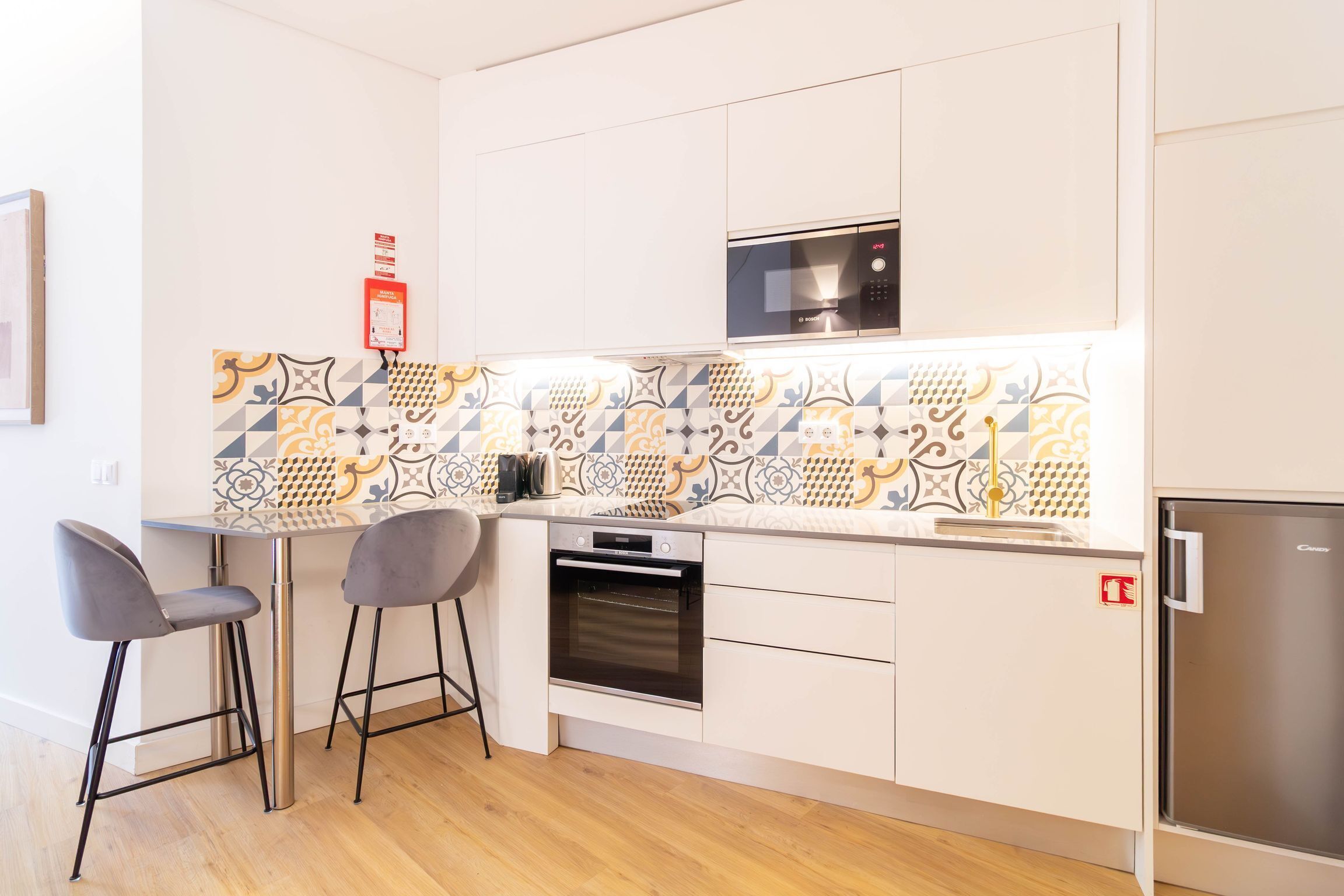 A modern kitchen with a microwave, oven, and refrigerator. There are two bar stools and a patterned backsplash.