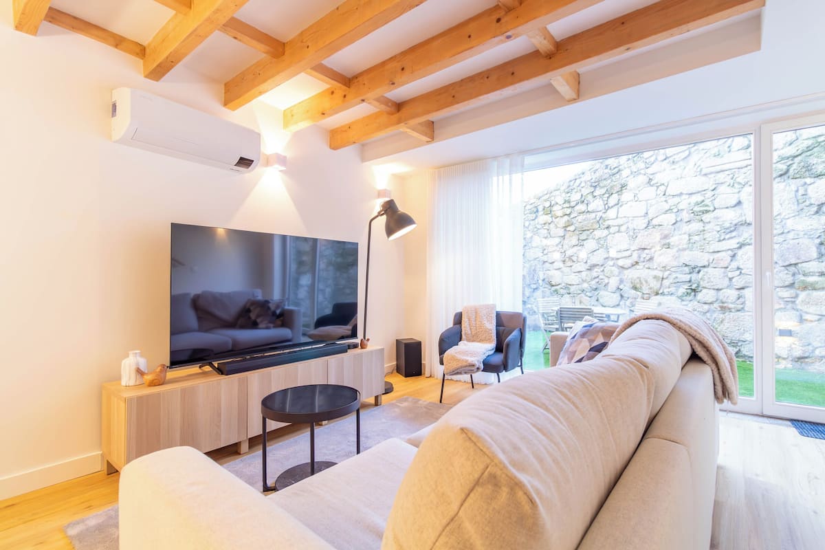 Una sala de estar moderna con una televisión de pantalla plana, vigas de madera, una pared de piedra y un ventanal grande.