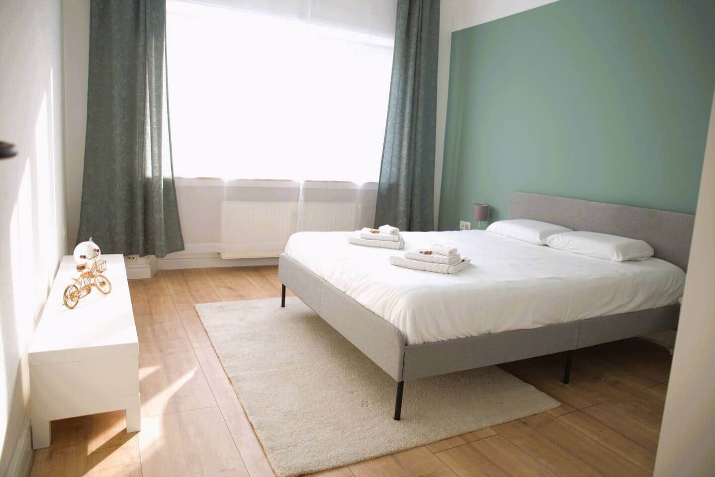 Un dormitorio moderno con una cama, una mesita de noche, un radiador y una ventana con cortinas.