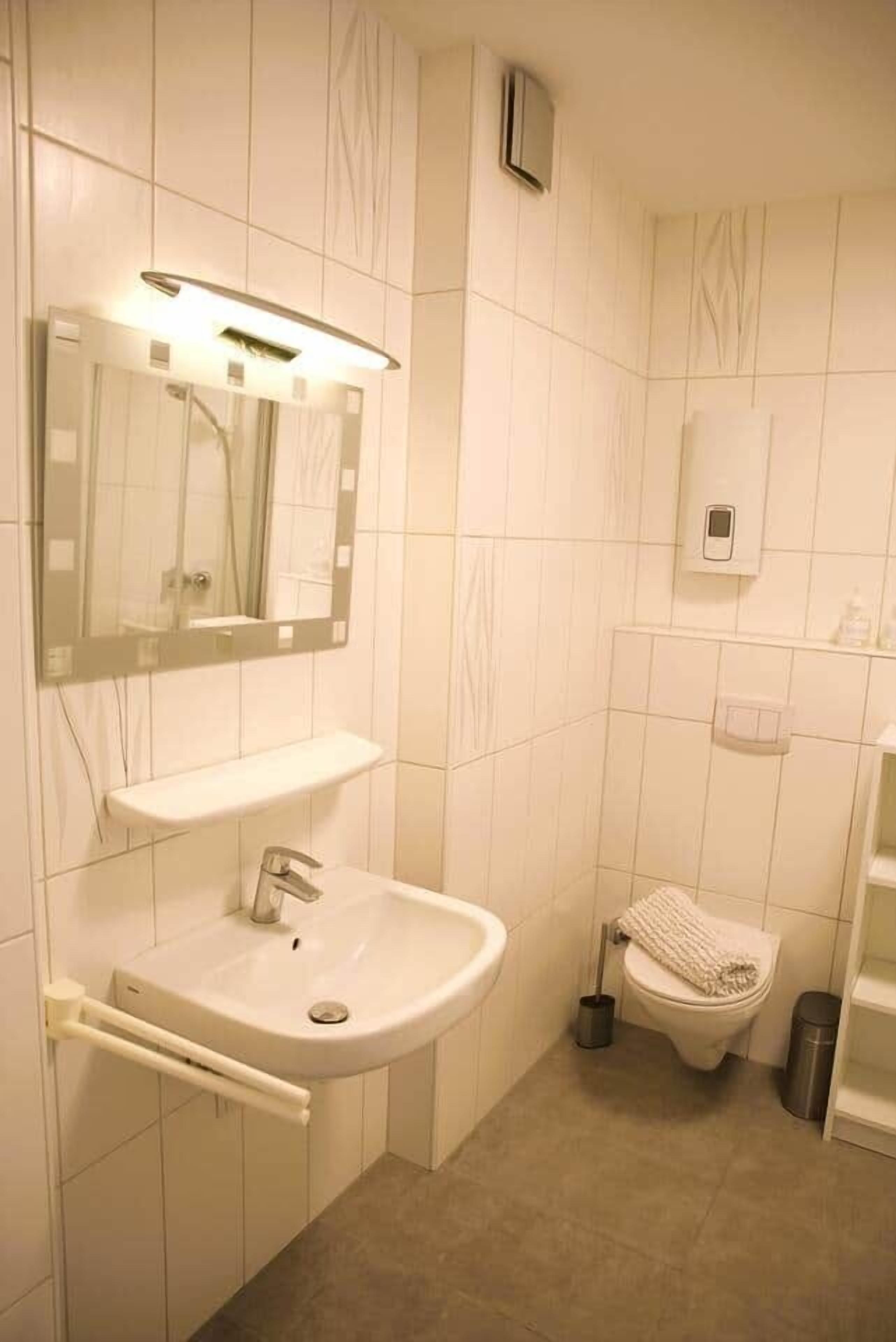 A small, modern bathroom with a white sink, mirror, and toilet.