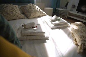 A neatly made bed with folded towels and a rolled-up towel, a small round tray with a bottle, and a white blanket on the right side. - Beautiful Cosy 2BR Apartment (Luxembourg City)