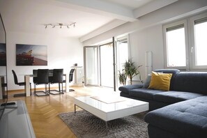A modern living room with a grey sofa, a white coffee table, and a dining area with a glass table and black chairs. - Charming Penthouse in the City Center (Luxembourg City)