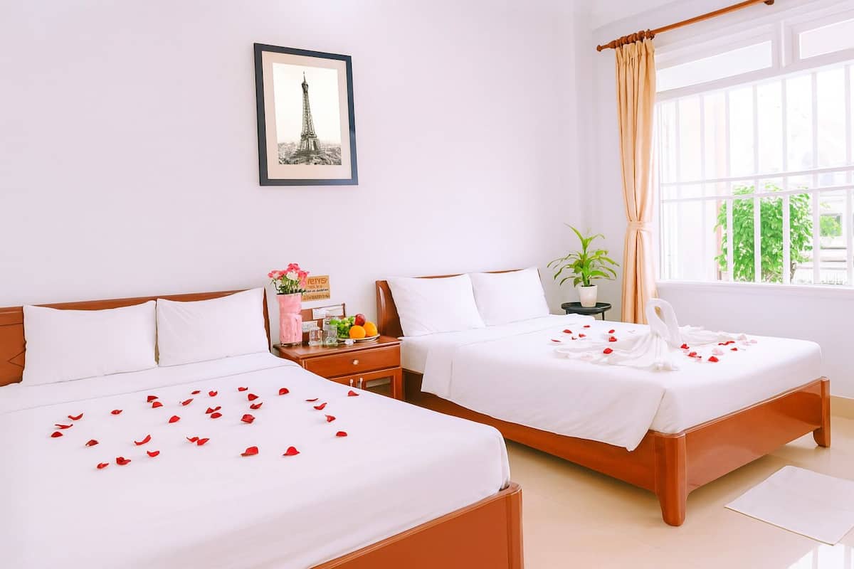 A hotel room with two beds, a framed picture of the Eiffel Tower, a potted plant, and a window with curtains.
