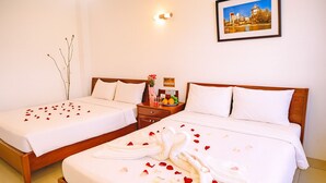 Een hotelkamer met twee bedden, een nachtkastje met een fruitschaal, een vaas met bloemen en een ingelijst foto aan de muur.