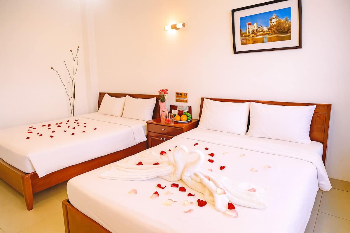 A hotel room with two beds, a nightstand with a fruit bowl, a vase with flowers, and a framed picture on the wall.