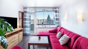 A modern living room with a red sofa, a wooden coffee table, a TV on a wooden stand, and a large window with curtains. - Apartment "Räuberhöhle" with Balcony and Wi-Fi (Goslar)