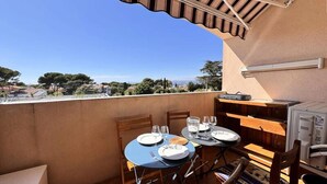 Un balcón con dos mesas listas para comer, una parrilla pequeña y vistas de la ciudad.