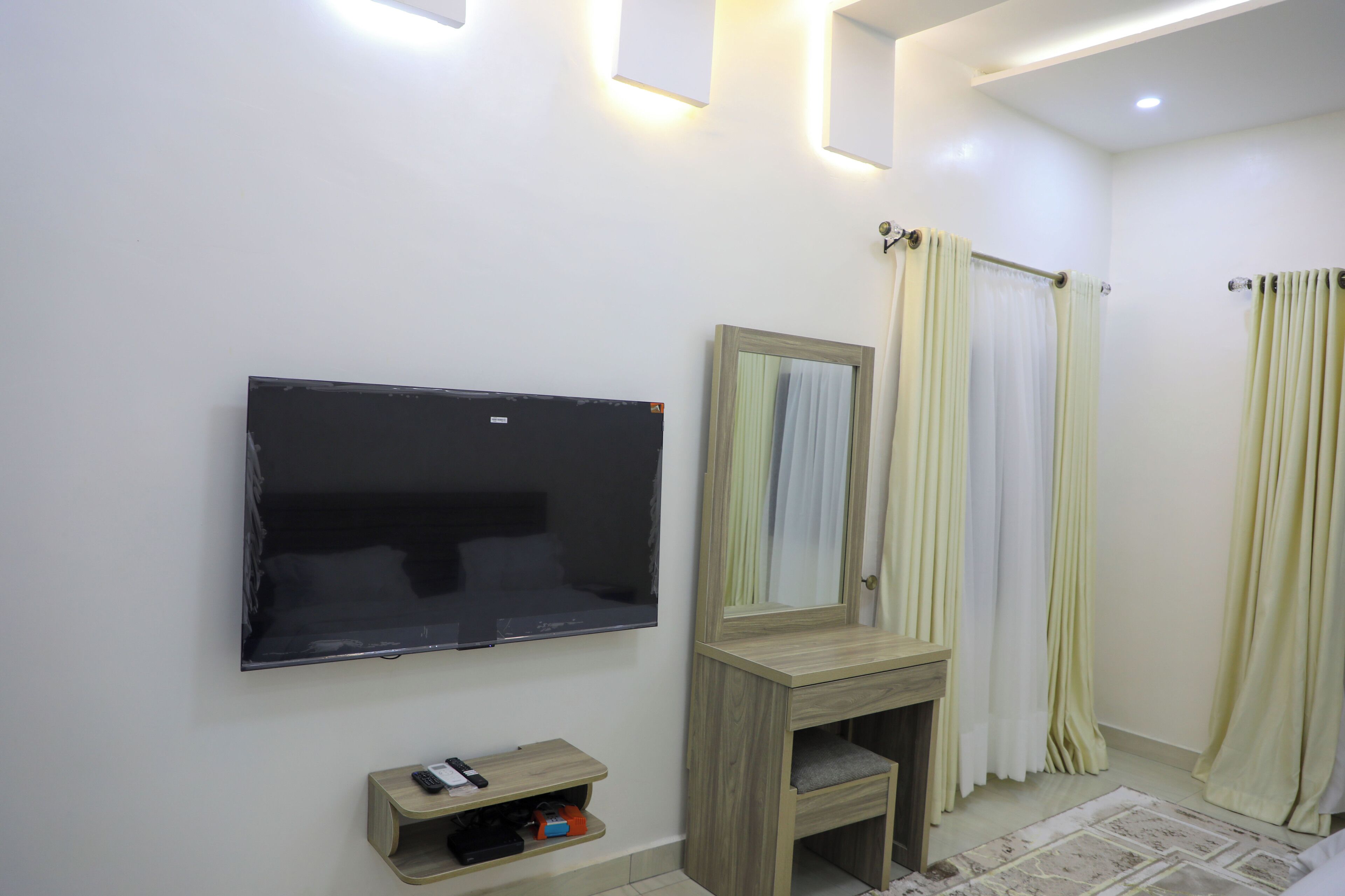 A bathroom with a mounted TV, a vanity with a mirror, and two sets of curtains.