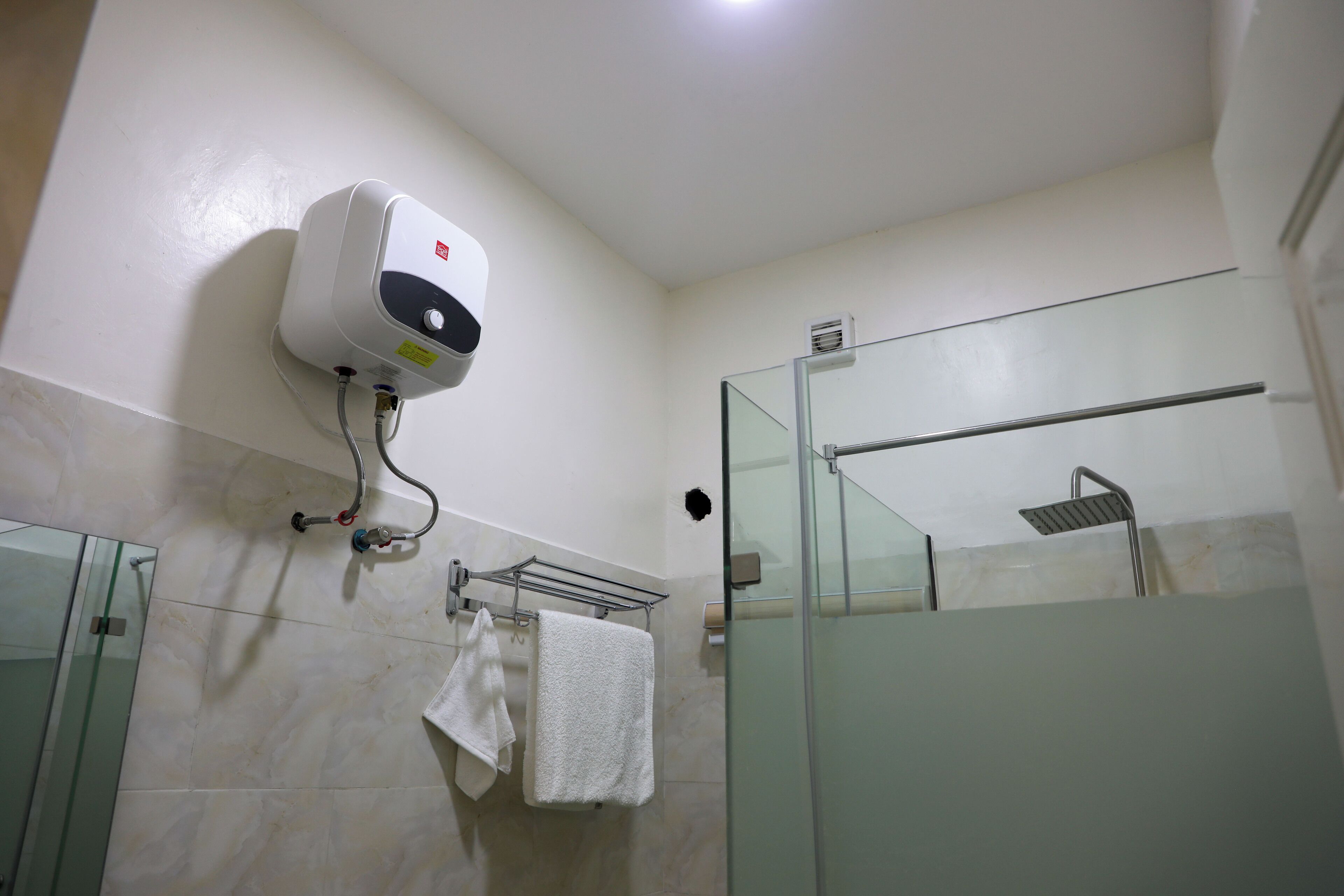 Un bagno con cabina doccia in vetro, un appendi asciugamani con due asciugamani e un asciugatore a muro.