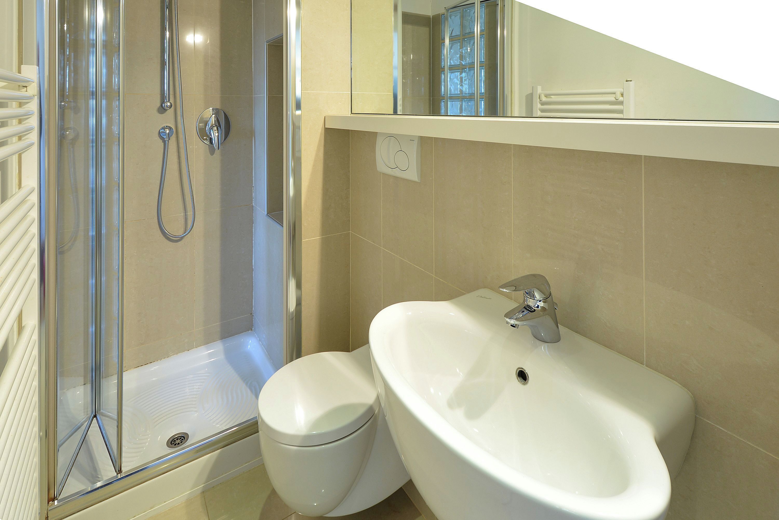 Ein modernes Badezimmer mit einer gläsernen Duschkabine, einer weißen Toilette und einem großen Waschbecken.
