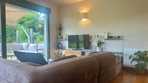 Een moderne woonkamer met een grote bank, een flatscreen televisie en een eethoek met een tafel en stoelen.