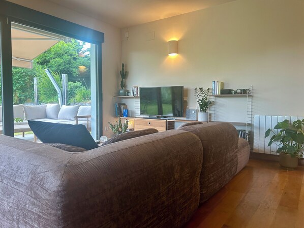 A modern living room with a large sofa, a flat-screen TV, and a dining area with a table and chairs.