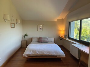 Une chambre à coucher avec un lit en bois, une table de chevet, une plante en pot et une fenêtre donnant sur des arbres.
