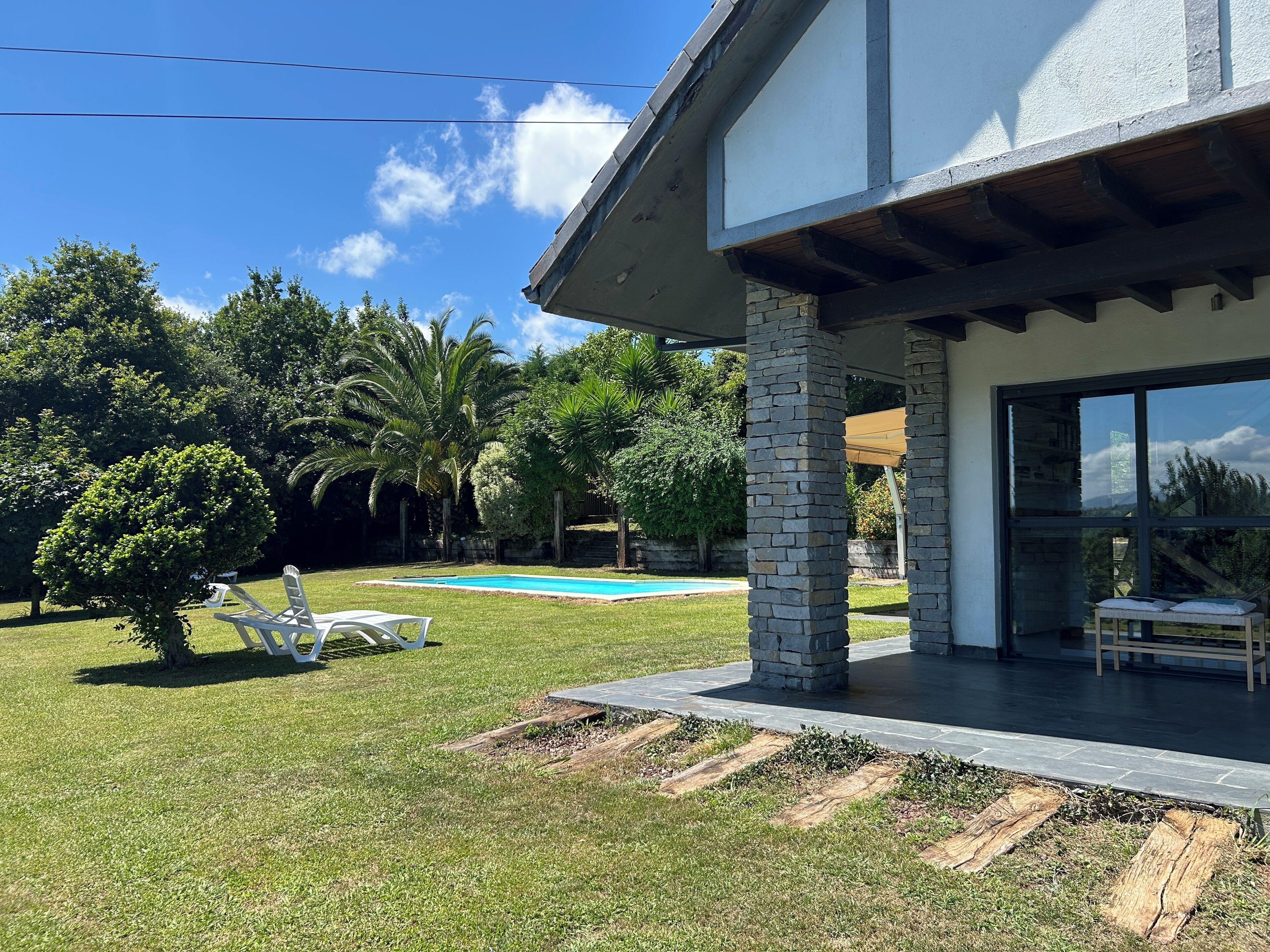 A modern house with a swimming pool, stone pillars, and a covered patio area.