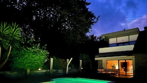 Een tweelaags huis met een zwembad, terras en een goed verlicht interieur.