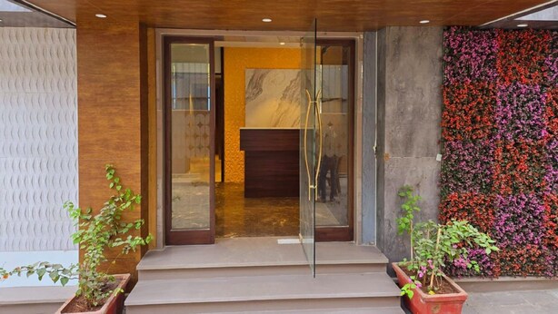 A modern building entrance with glass doors, a wooden overhang, and a flower wall. - THE BOHOO 99 (Mumbai)