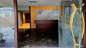 A modern reception area with a marble wall, wooden reception desk, and a glass partition with a gold accent. - THE BOHOO 99 (Mumbai)
