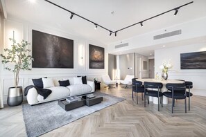 A modern living room with a sofa, coffee table, and dining area with chairs. - Premium Suite 3 BR with 200° Views of Burj Khalifa, Sunset Views and 85" TV! (Dubai)