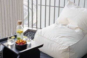 A balcony with a white cushioned chair, a tray with a bottle of water, glasses, and a bowl of fruit. - Premium Suite 3 BR with 200° Views of Burj Khalifa, Sunset Views and 85" TV! (Dubai)