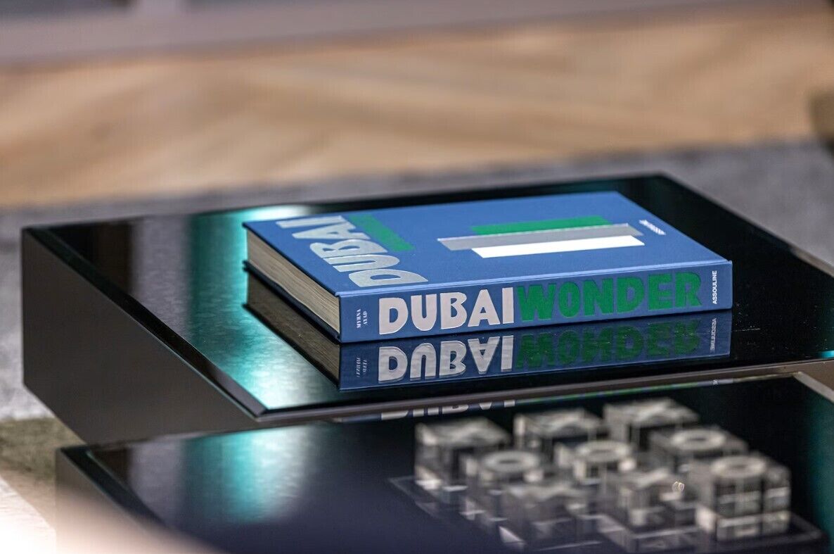 Una pila de libros con el título 'Dubai Wonder' sobre una superficie reflectante.