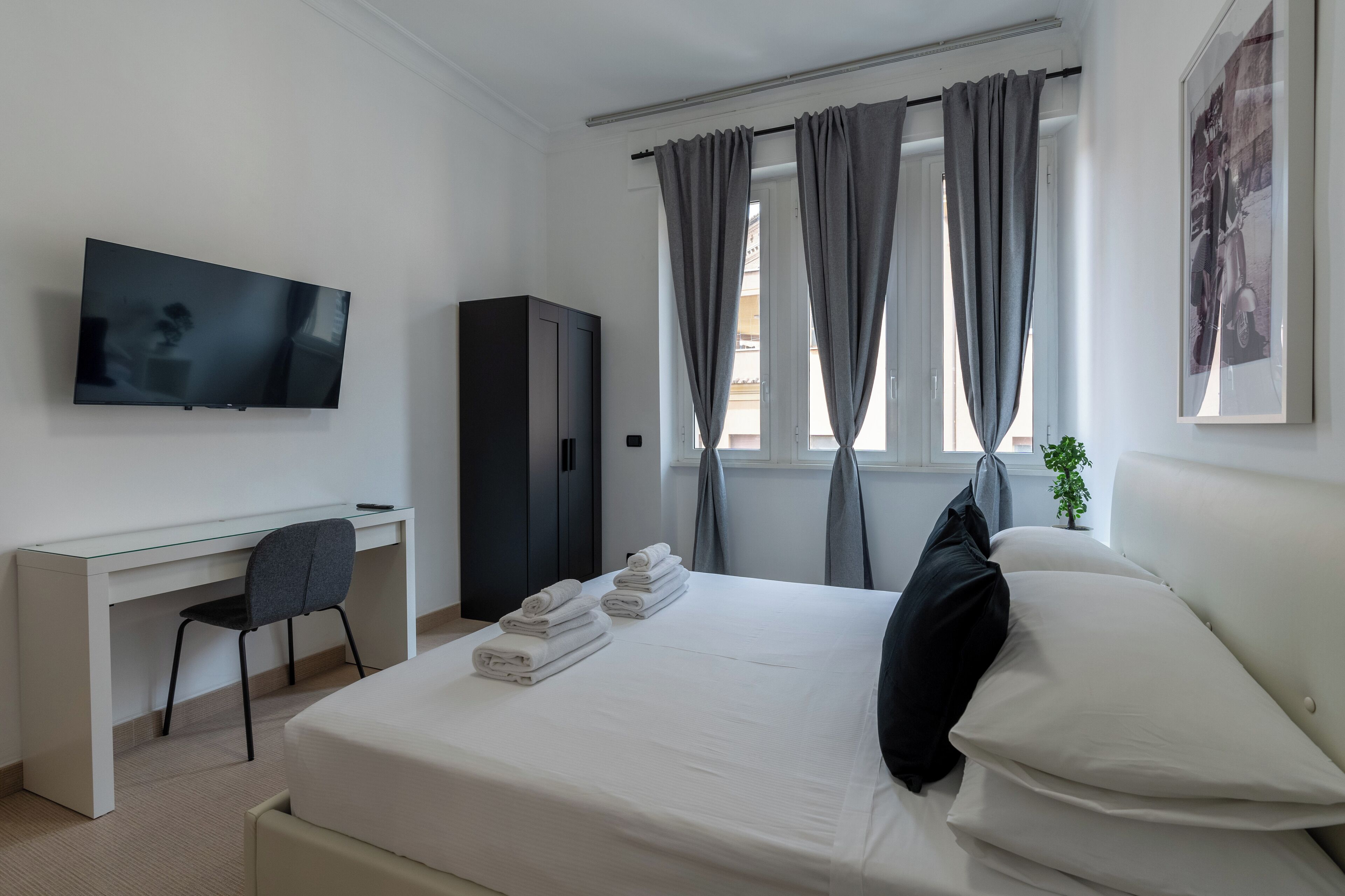 A hotel room with a bed, a desk, a chair, a television, and a window with curtains.