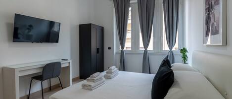 A hotel room with a bed, a desk, a chair, a television, and a window with curtains.