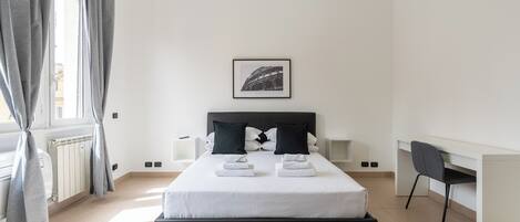 A modern bedroom with a bed, bedside tables, a desk, and a framed picture on the wall.