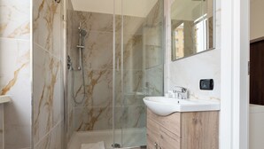 Un baño moderno con ducha de vidrio, lavamanos blanco y muebles de madera.