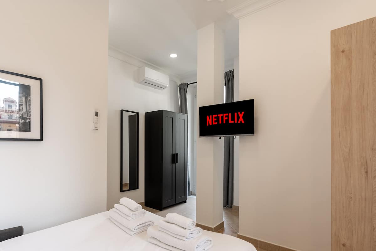 A hotel room with a bed, a TV mounted on the wall, a wardrobe, and a framed picture on the wall.
