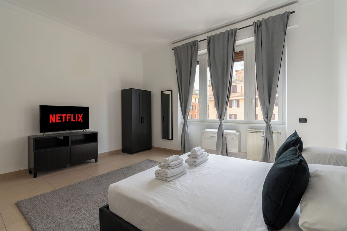 A hotel room with a bed, a TV displaying 'NETFLIX', a wardrobe, and a window with curtains.