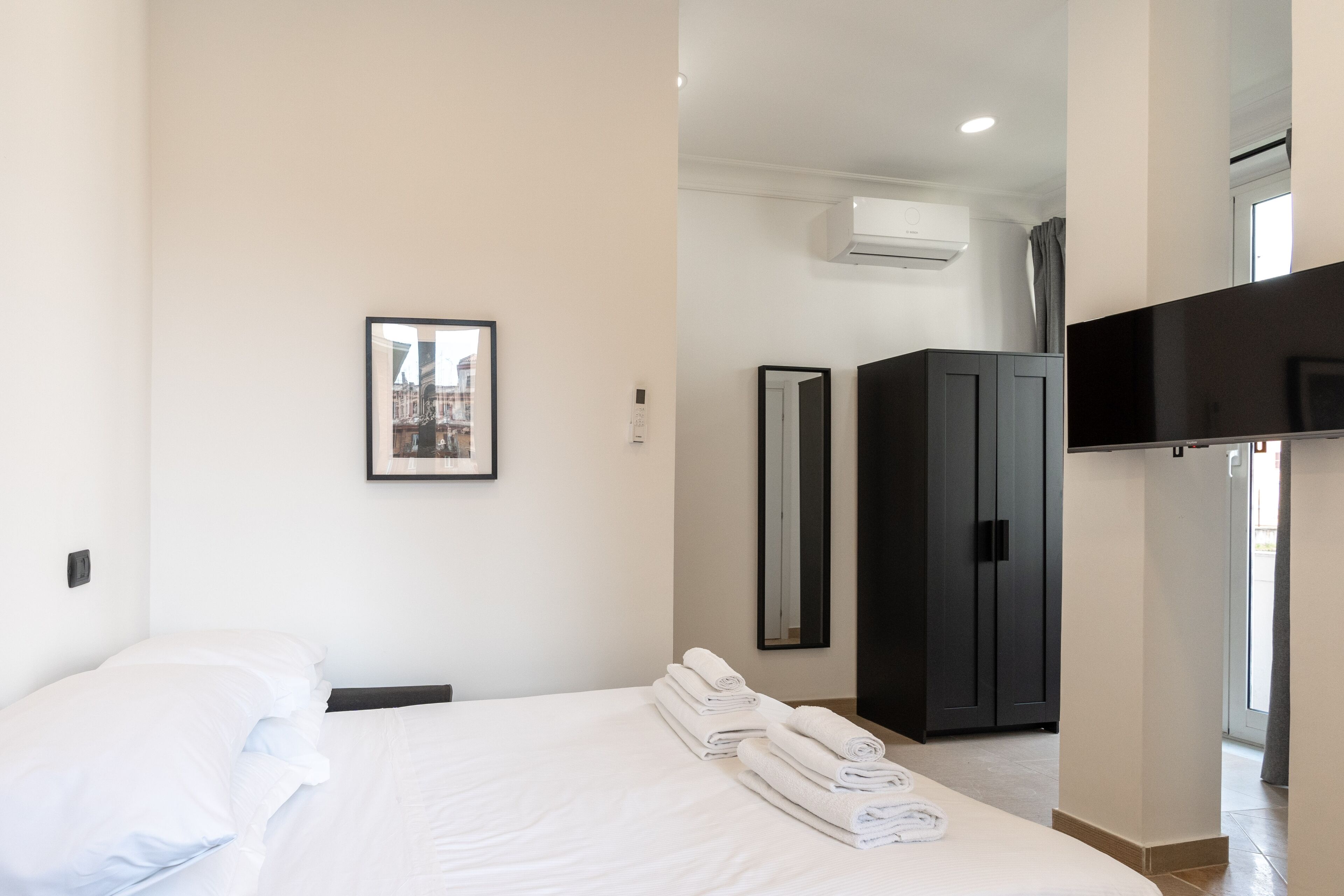A hotel room with a bed, a wardrobe, a television, and a framed picture on the wall.