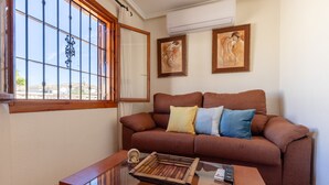 Una sala de estar con un sofá marrón, una mesa de centro de vidrio y una ventana con barrotes.