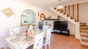 Una cocina moderna con armarios blancos, una mesa de comedor con platos y un televisor sobre un mueble.